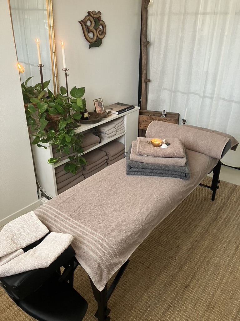 Massagebänk med ljus, handdukar och gröna växter